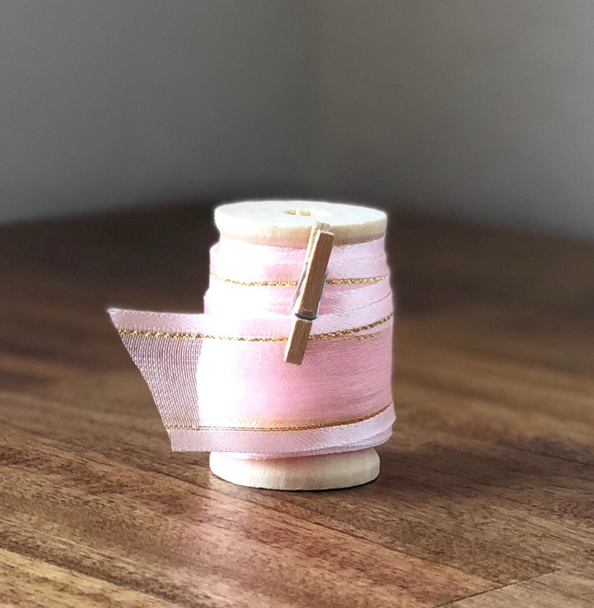 Blush pink organza ribbon with gold edge on wooden spool