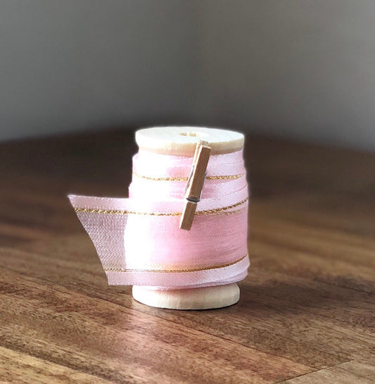 Blush pink organza ribbon with gold edge on wooden spool
