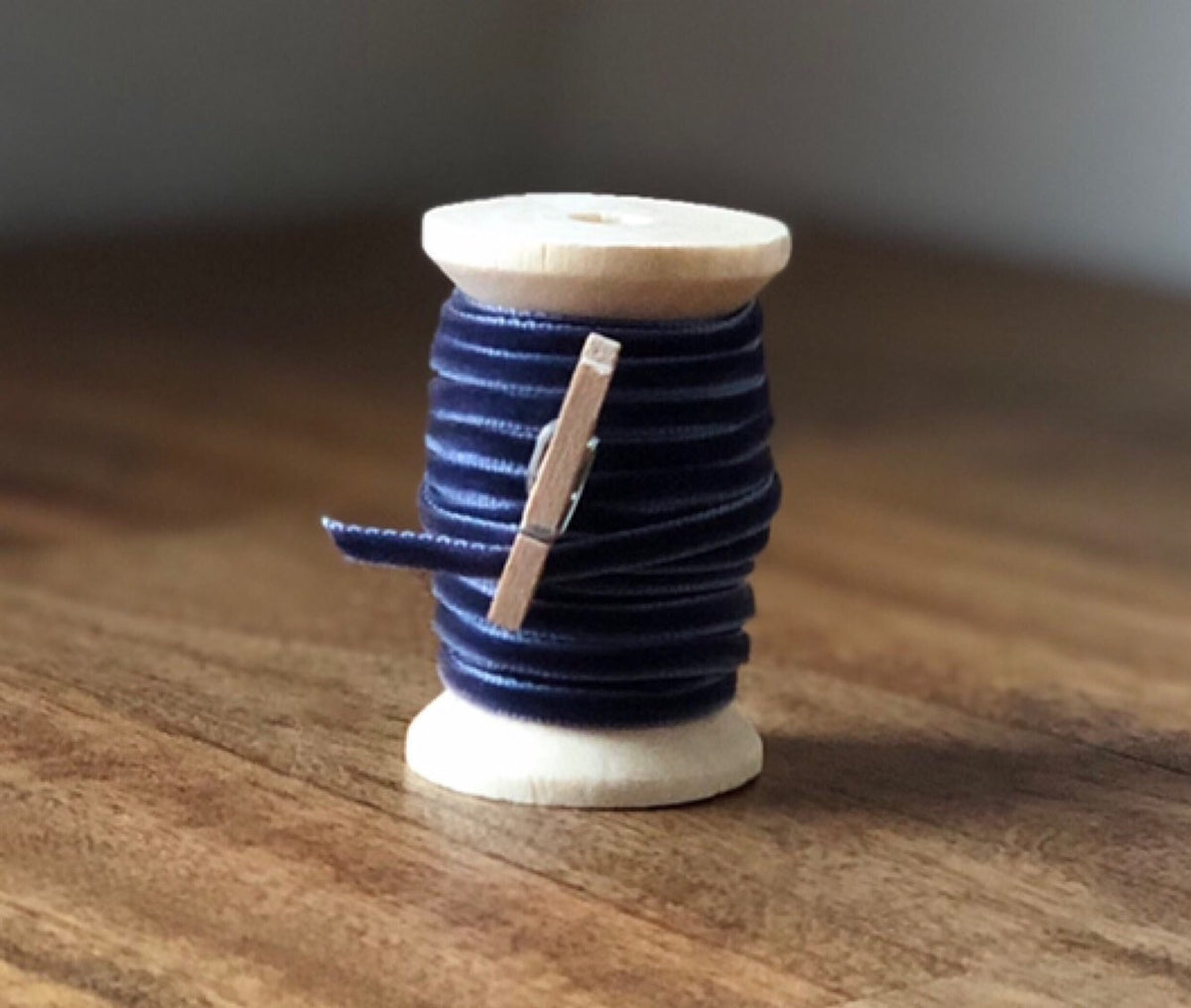 Thin navy blue velvet ribbon on wooden spool, view 2