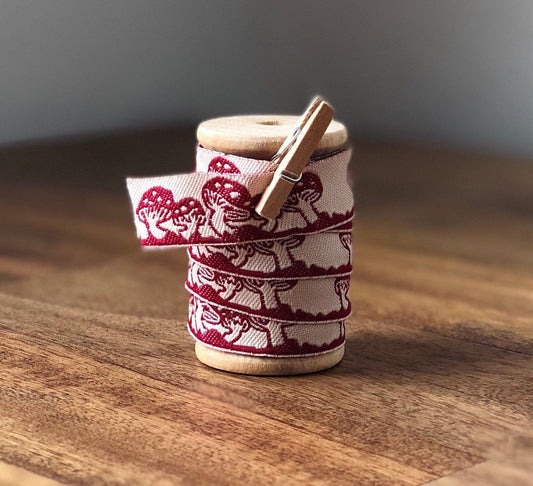 Embroidered red and white mushroom ribbon on wooden spool